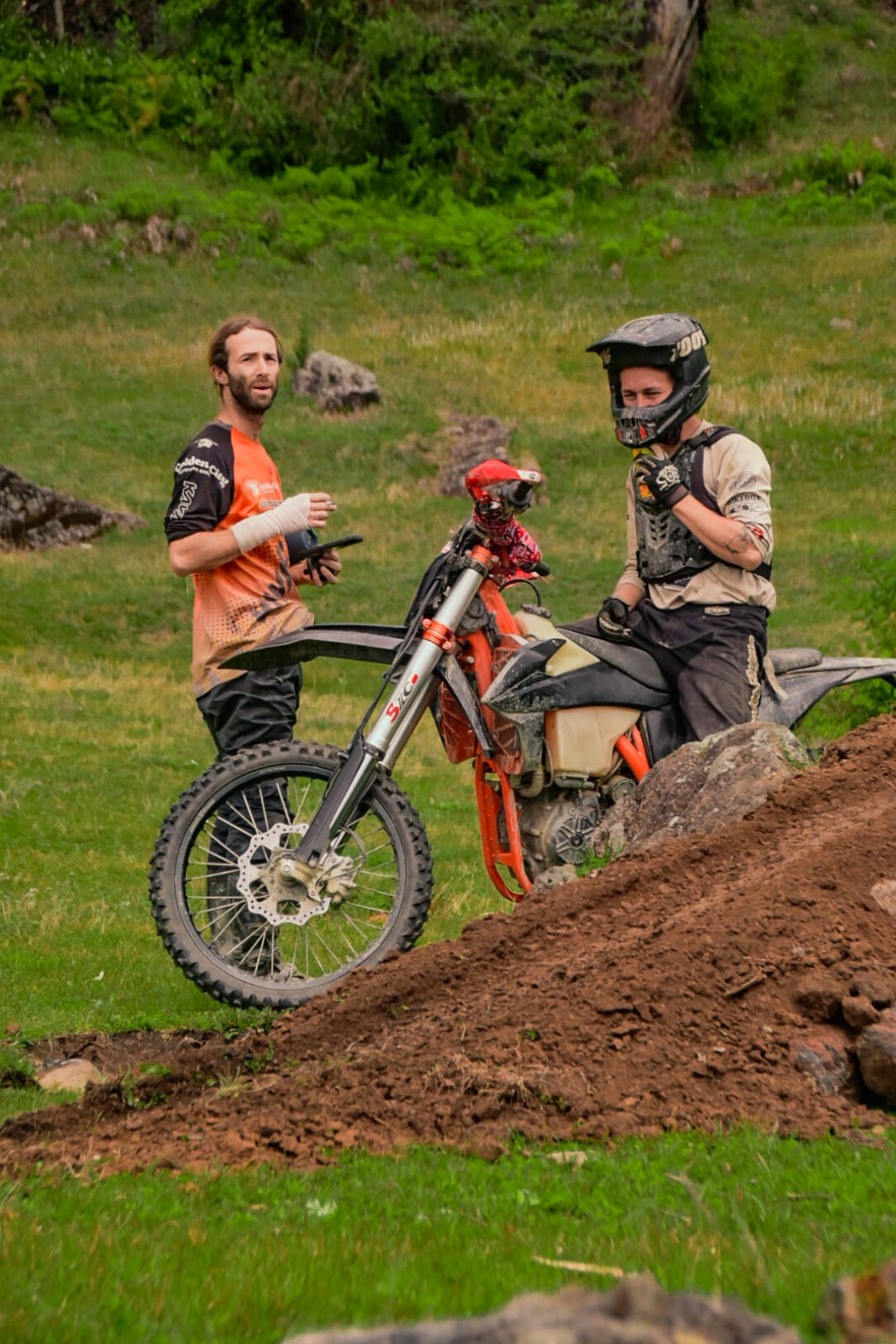Two riders taking a break beside a bike on a grassy trail